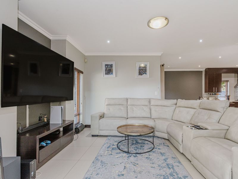A well-maintained living room featuring tiled flooring, recessed downlighting, and crown molding, with an open-plan flow leading toward the kitchen area.