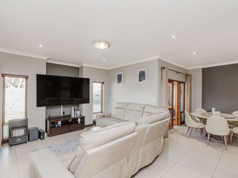 Spacious open-plan living and dining area featuring neutral tiled flooring, recessed lighting, and timber-framed glass doors leading to the exterior.