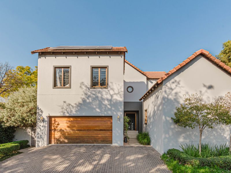 A well-maintained double-story residence featuring a paved driveway, wooden garage door, and solar panels on a tiled roof.
