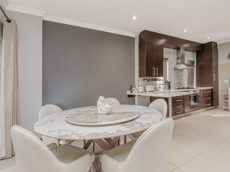 Open-plan kitchen and dining area featuring modern dark wood cabinetry, built-in appliances, tiled flooring, and a neutral color palette.