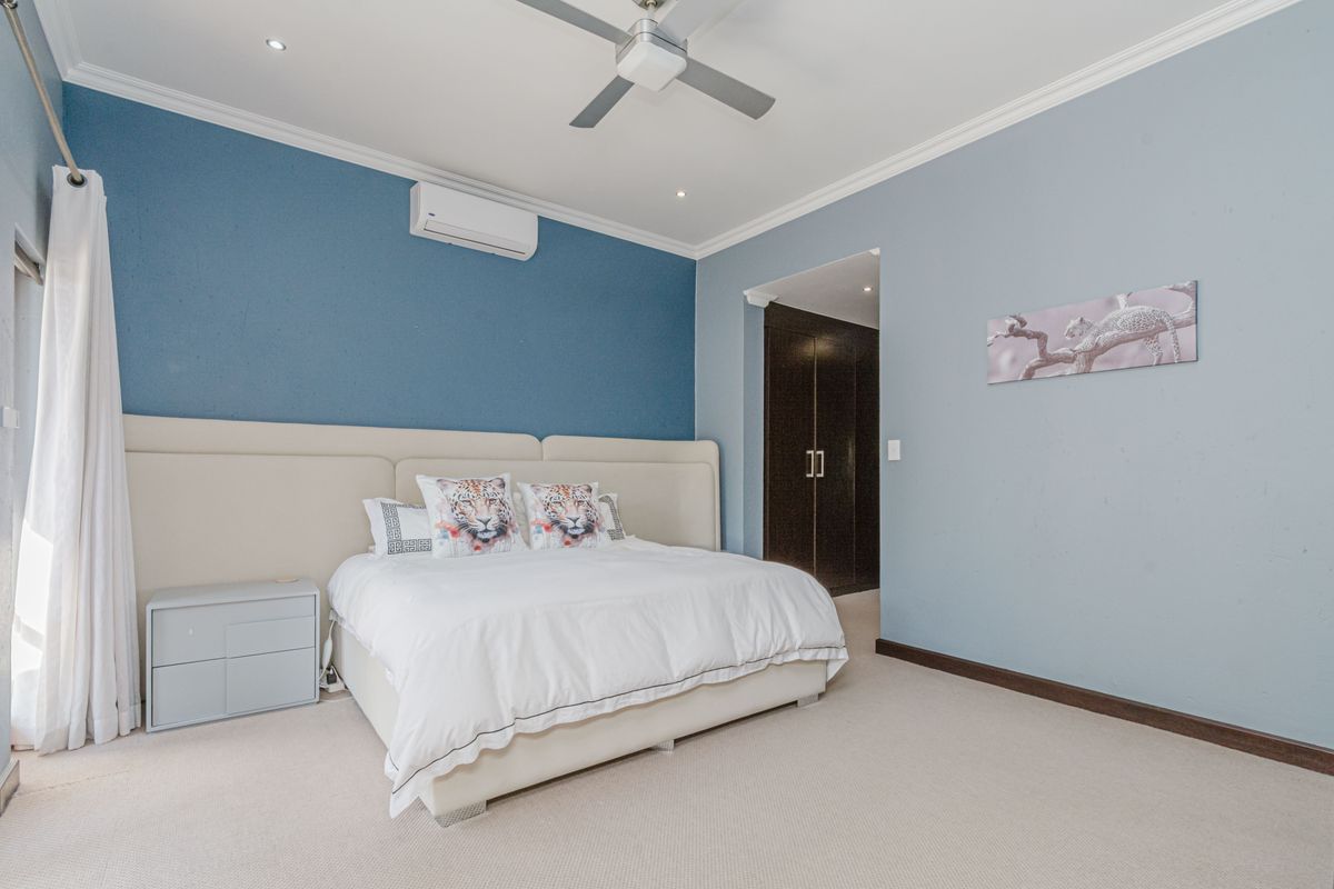 Spacious bedroom featuring a split-system air conditioner, ceiling fan, recessed lighting, and built-in cupboards with a neutral carpet finish.