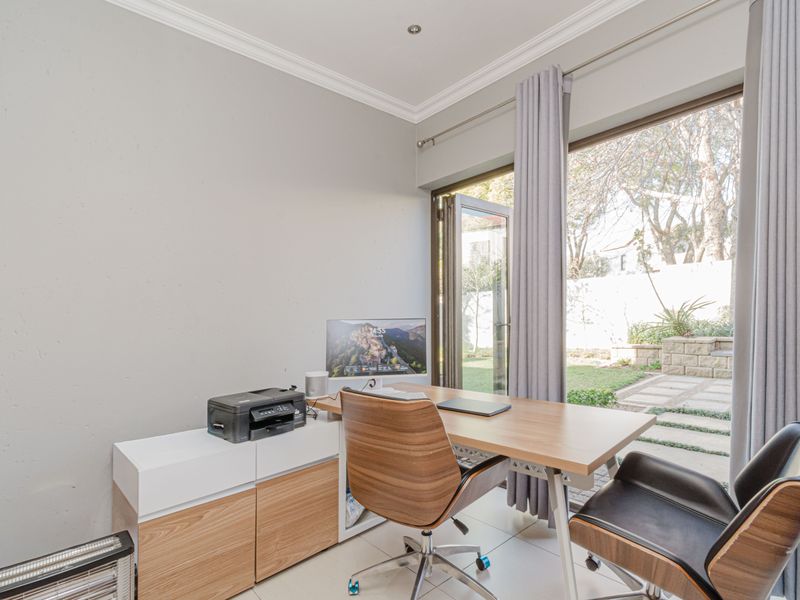 A bright home office featuring tiled flooring, recessed lighting, and a large sliding glass door providing direct access to the garden.