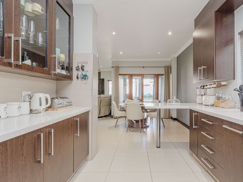 Modern kitchen featuring dark wood cabinetry, stone countertops, and a breakfast bar, flowing into an open-plan dining area with tiled flooring throughout.