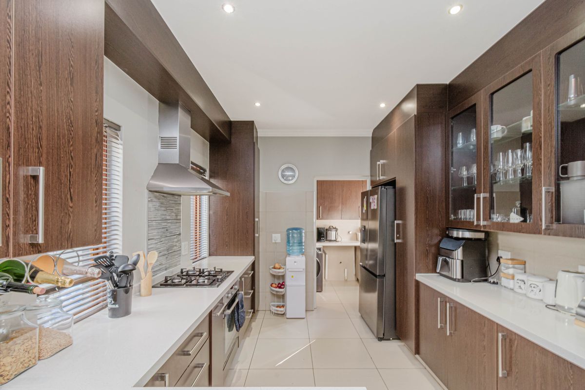Modern kitchen featuring dark wood cabinetry, stone countertops, gas hob, extractor fan, and integrated storage with a seamless flow into the adjacent scullery area.