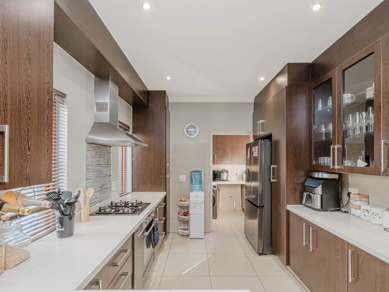 Modern kitchen featuring dark wood cabinetry, stone countertops, gas hob, extractor fan, and integrated storage with a seamless flow into the adjacent scullery area.