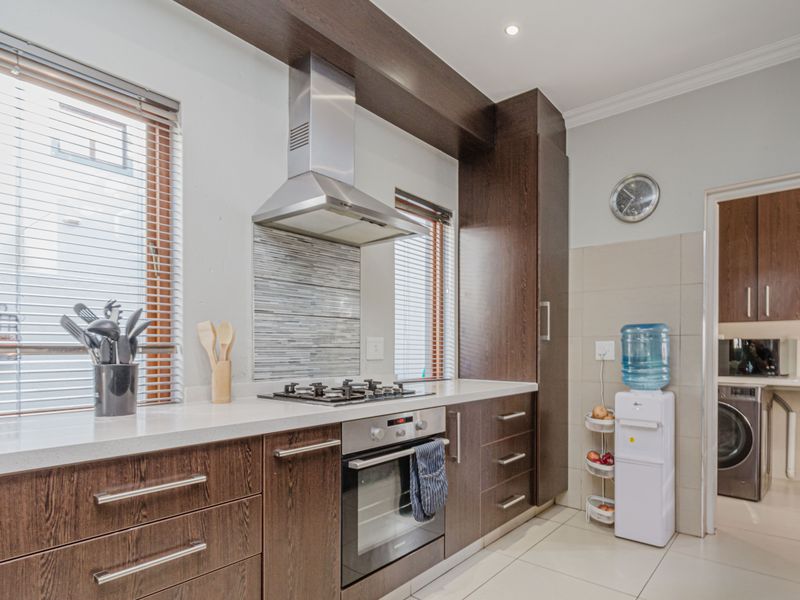 Modern kitchen featuring dark wood cabinetry, stone countertops, a gas hob with stainless steel extractor, and tiled flooring, with an adjacent laundry area.