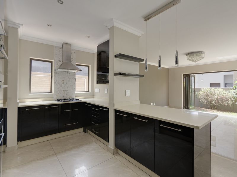 Modern open-plan kitchen featuring sleek black cabinetry, stone countertops, gas hob, and seamless flow to the outdoor patio area.