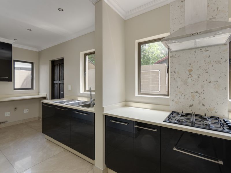 Modern kitchen featuring high-gloss black cabinetry, stone countertops, a gas hob with extractor fan, and a stylish terrazzo-style splashback.