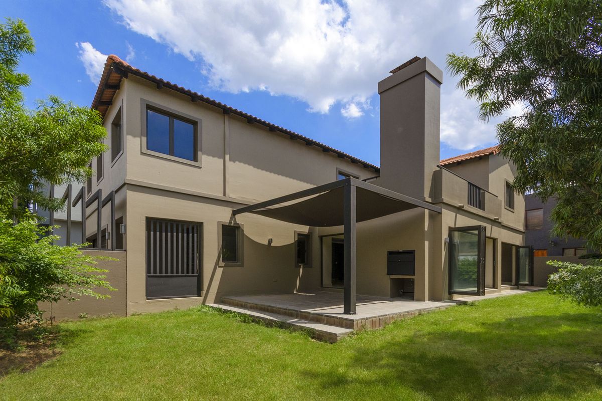 Rear view of the cluster home featuring a covered patio with a built-in braai, bi-fold doors, and a well-maintained garden.