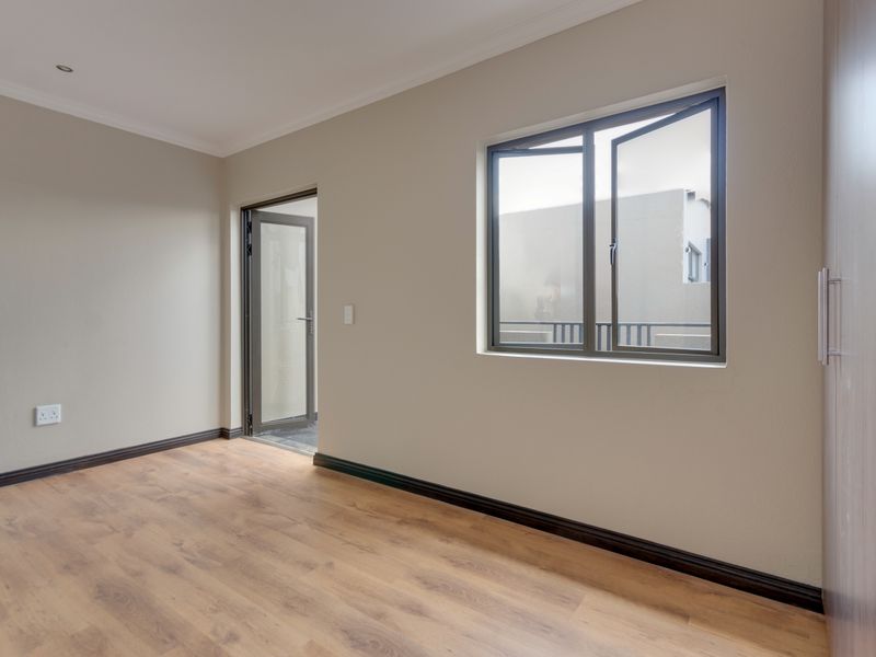 A clean, empty bedroom featuring modern laminate flooring, built-in cupboards, and neutral wall finishes with access to an outdoor area.