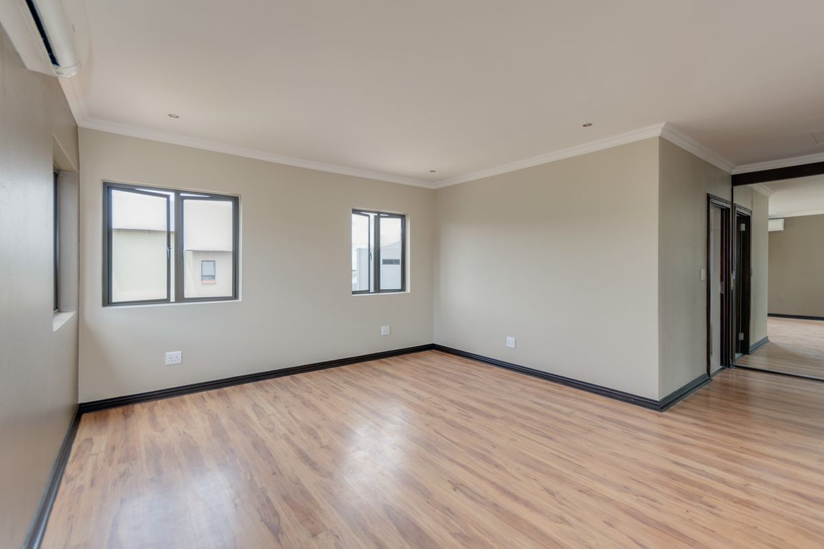A spacious, empty bedroom featuring laminate flooring, built-in cupboards, and an air conditioning unit, finished with neutral walls and modern aluminium window frames.