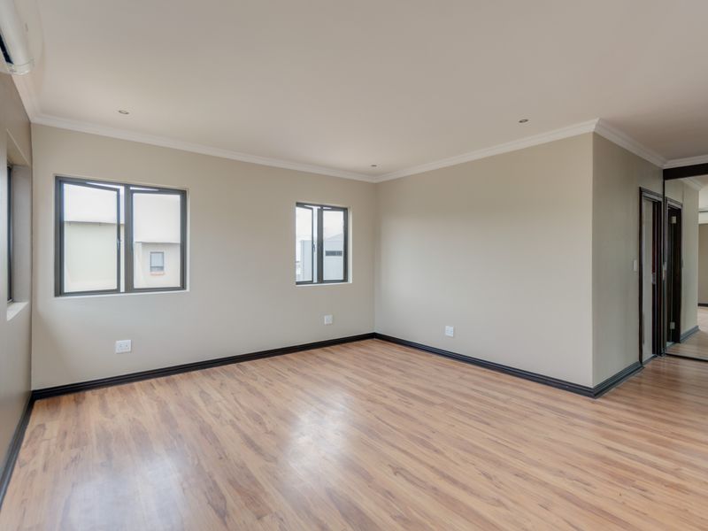 A spacious, empty bedroom featuring laminate flooring, built-in cupboards, and an air conditioning unit, finished with neutral walls and modern aluminium window frames.
