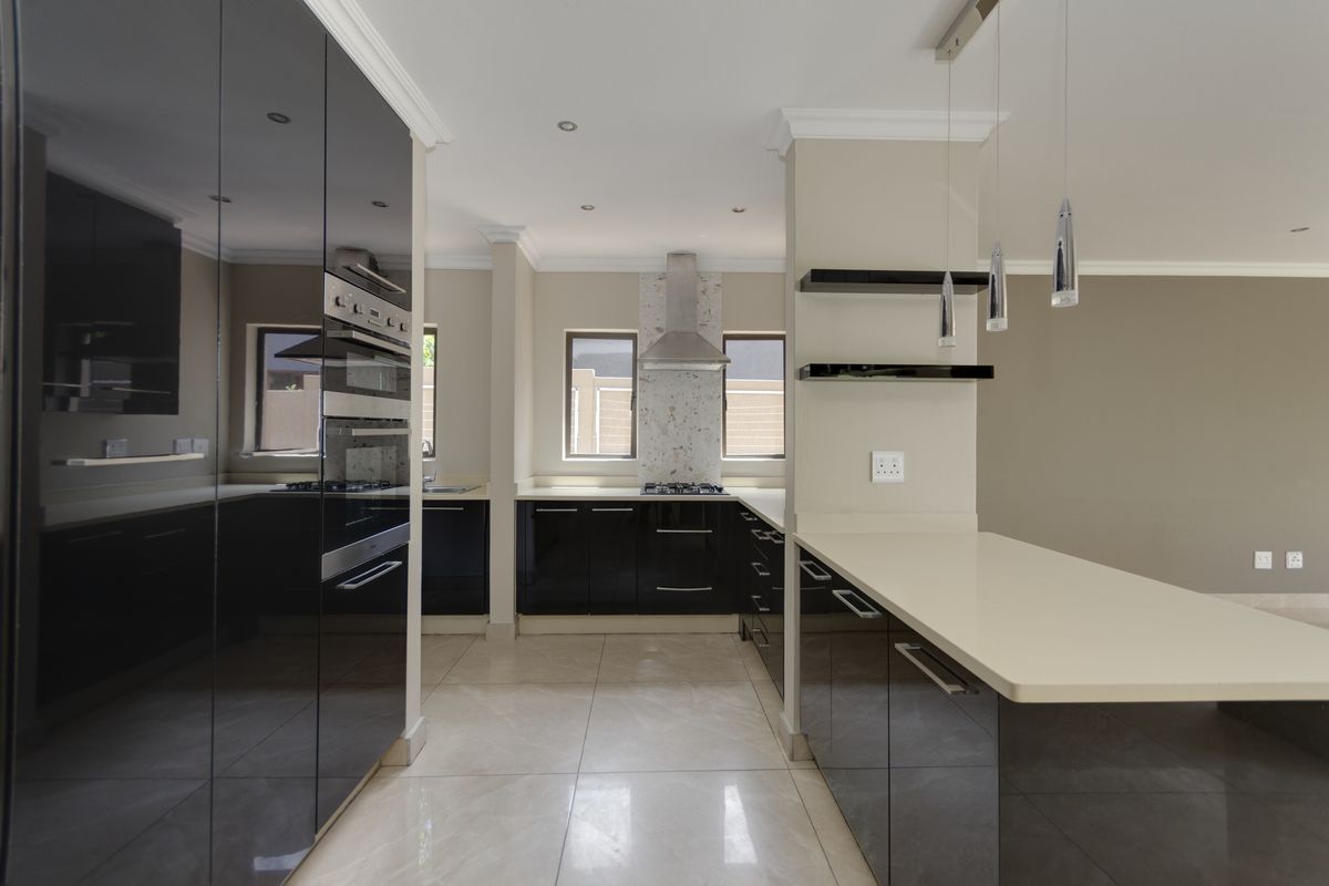 Modern kitchen featuring high-gloss black cabinetry, stone countertops, built-in oven, gas hob, and sleek pendant lighting in an open-plan layout.