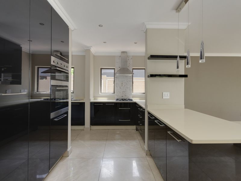 Modern kitchen featuring high-gloss black cabinetry, stone countertops, built-in oven, gas hob, and sleek pendant lighting in an open-plan layout.