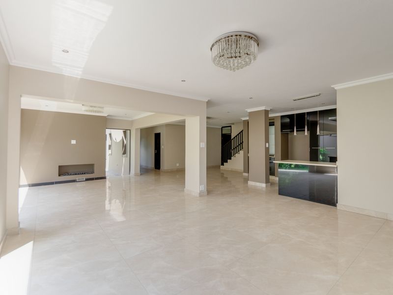 Spacious open-plan living area featuring polished porcelain tiles, a modern kitchen island, recessed fireplace, and elegant chandelier lighting in a neutral color palette.