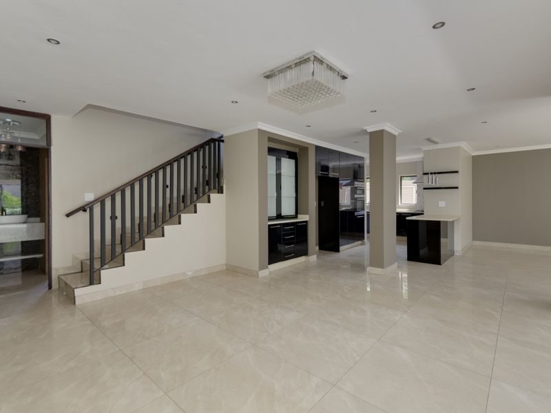 Spacious open-plan living area featuring polished porcelain tiles, a modern staircase, and a sleek kitchen with built-in cabinetry and a central island.