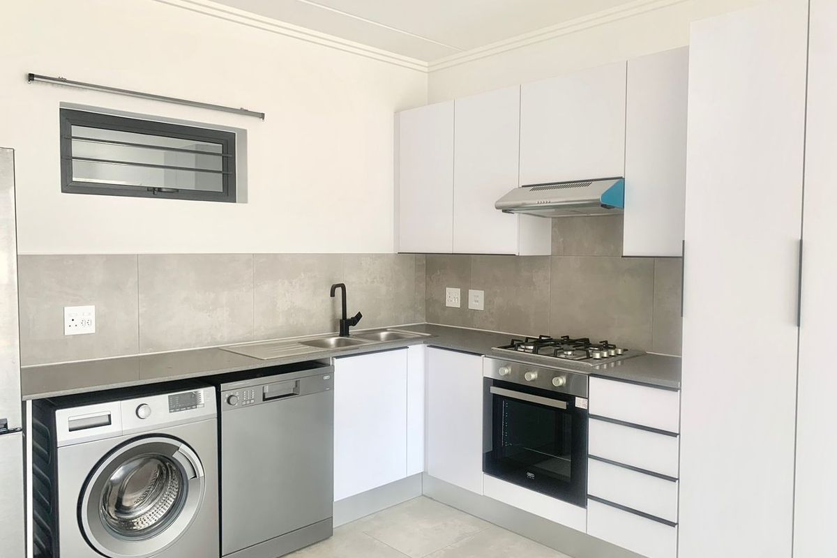 Modern kitchen featuring white cabinetry, gas hob, electric oven, extractor fan, stainless steel sink, and tiled backsplash with neutral floor tiles.