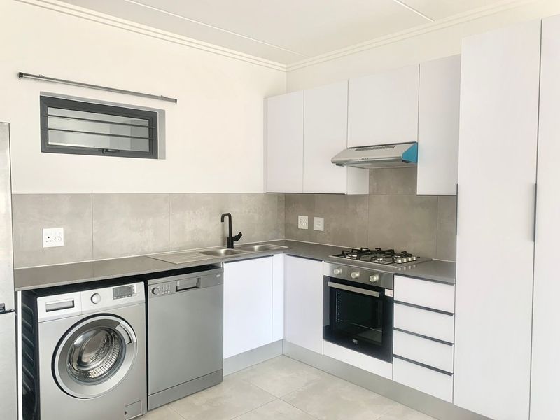 Modern kitchen featuring white cabinetry, gas hob, electric oven, extractor fan, stainless steel sink, and tiled backsplash with neutral floor tiles.