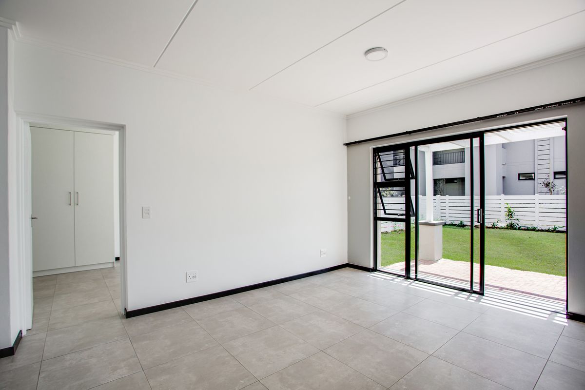 Bright and spacious living area featuring neutral tiled flooring, a built-in cupboard, and large sliding glass doors providing direct access to the garden.