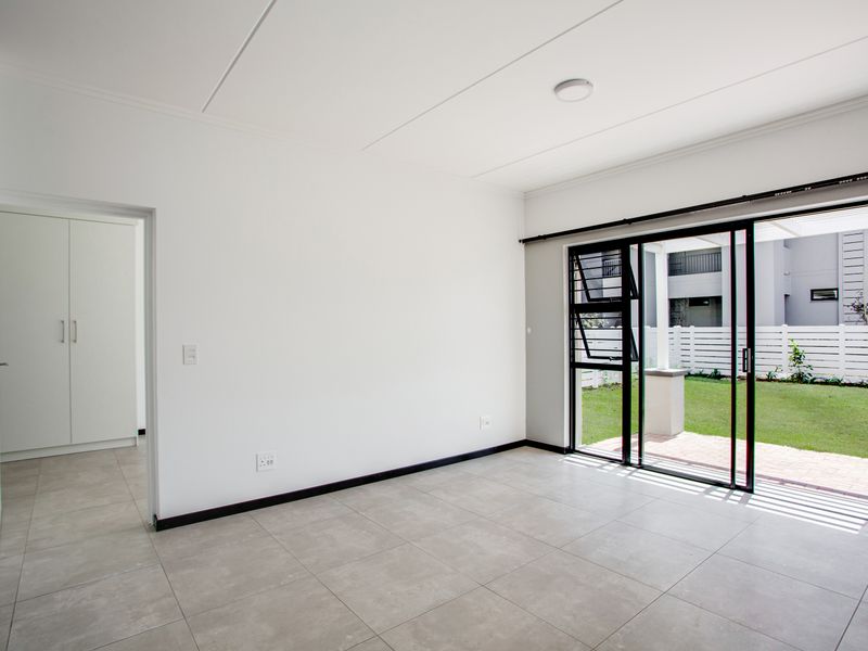 Bright and spacious living area featuring neutral tiled flooring, a built-in cupboard, and large sliding glass doors providing direct access to the garden.
