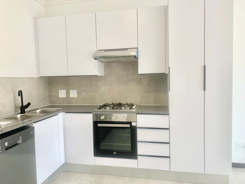 Modern kitchen featuring white cabinetry, stone countertops, a gas hob, electric oven, extractor fan, and integrated dishwasher.