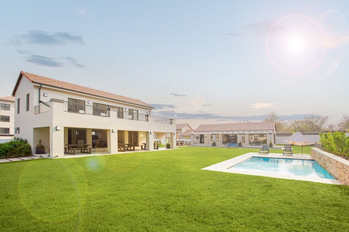 Spacious rear exterior featuring a well-maintained lawn, a swimming pool, and a multi-level building with a covered patio and upper-level balcony.