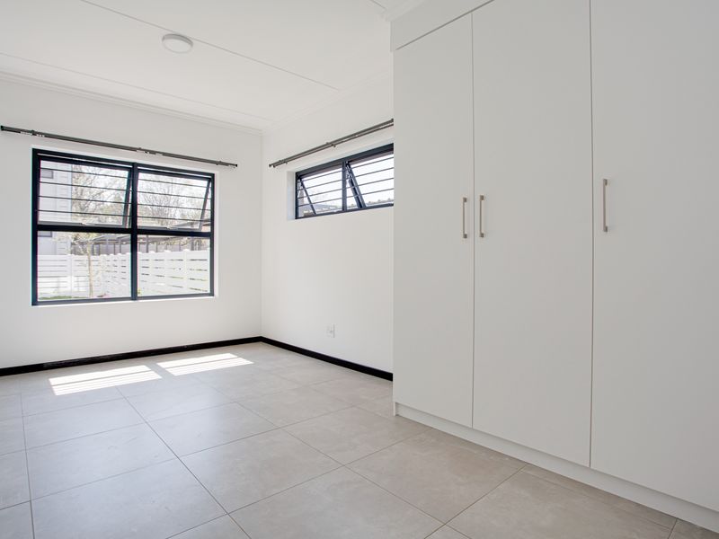 A bright, empty bedroom featuring modern tiled flooring, built-in cupboards, and large windows with security bars.