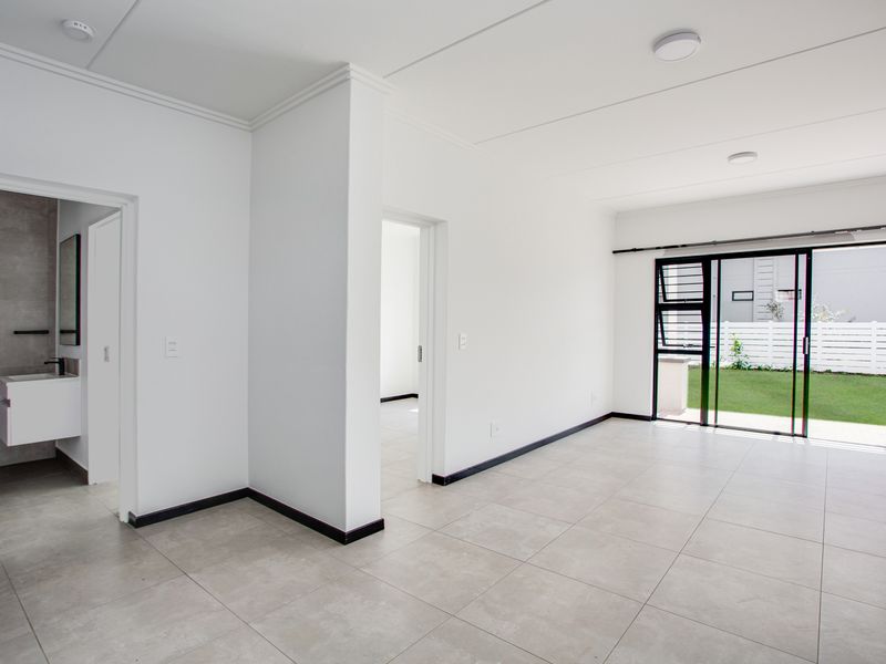 Bright open-plan living area featuring neutral tiled flooring, modern finishes, and direct access to a private garden through sliding glass doors.