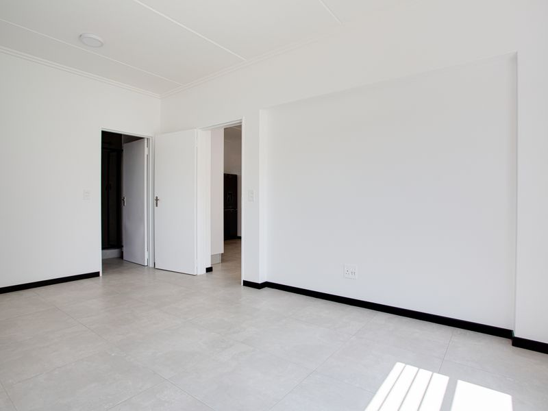 A bright, empty living area featuring neutral tiled flooring, clean white walls, and modern skirting boards, providing a versatile blank canvas for interior design.