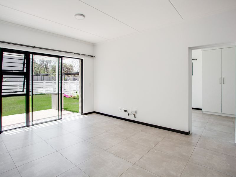 Bright and spacious open-plan living area featuring neutral tiled flooring, large sliding glass doors leading to the garden, and access to built-in storage.
