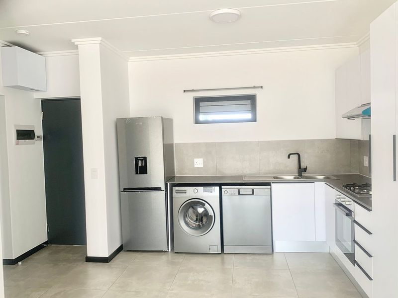 Modern kitchen featuring white cabinetry, stainless steel appliances, tiled backsplash, gas hob, and integrated oven, complemented by neutral floor tiles.