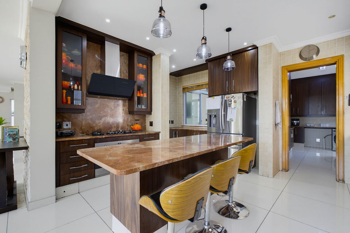 Modern kitchen featuring dark wood cabinetry, granite countertops, a central island, and high-quality built-in appliances, with an adjacent scullery area visible.
