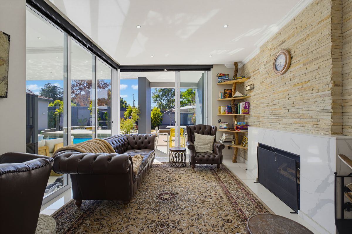 A bright living room featuring a stone fireplace, marble hearth, and large sliding glass doors that provide seamless access to the outdoor pool area.