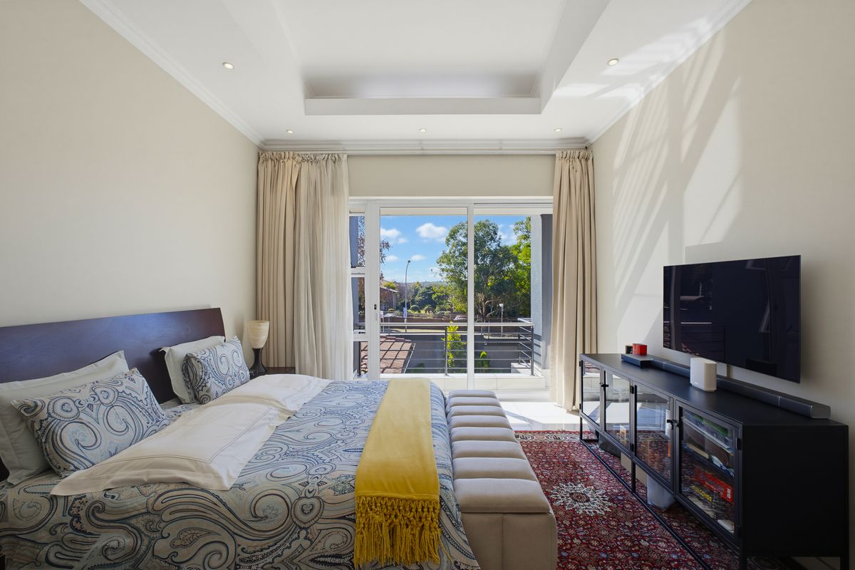 Spacious bedroom featuring a tray ceiling, recessed lighting, and a sliding glass door providing access to a private balcony with exterior views.