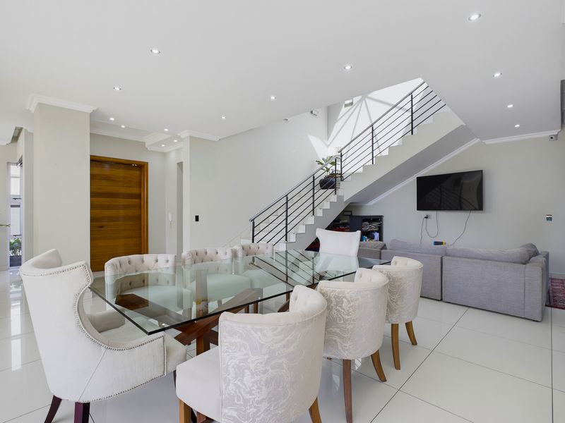 Spacious open-plan living and dining area featuring polished porcelain tiles, recessed lighting, and a modern staircase with a metal balustrade.