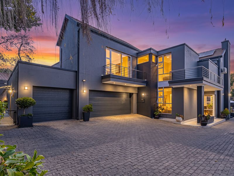 Modern double-storey residence featuring a dark facade, double garage, paved driveway, and upper-level balconies, presented in excellent condition at twilight.