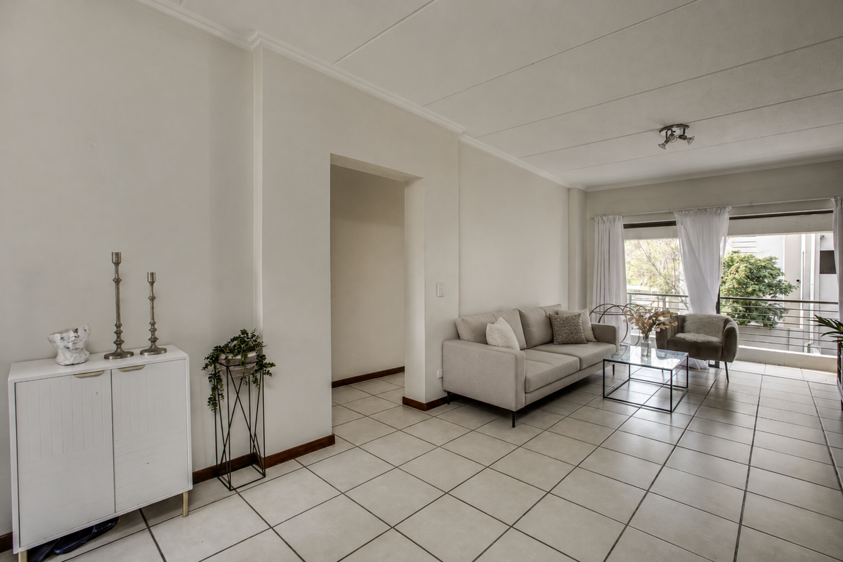 A bright and spacious living room featuring neutral tiled flooring and direct access to a private balcony through large sliding glass doors.