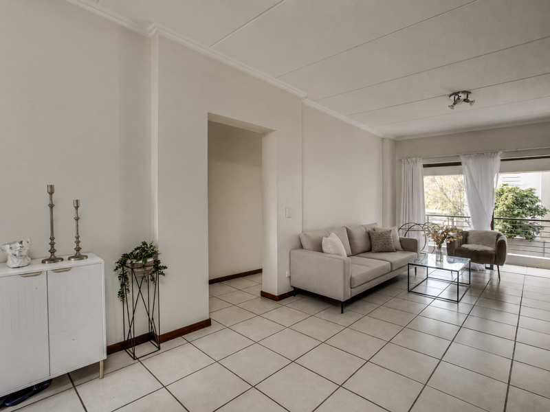 A bright and spacious living room featuring neutral tiled flooring and direct access to a private balcony through large sliding glass doors.