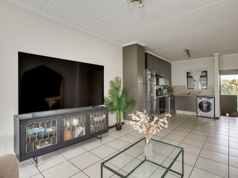 Open-plan living area featuring tiled flooring and a functional kitchen with built-in cabinetry, integrated appliances, and a tiled backsplash.