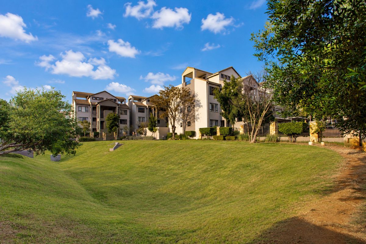 A view of the rear elevation of a multi-story apartment complex featuring well-maintained landscaped grounds and perimeter fencing.