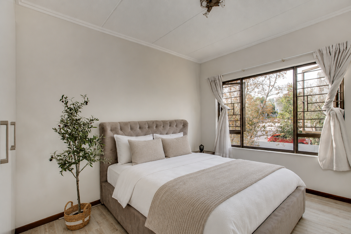 A well-lit bedroom featuring neutral walls, laminate flooring, a built-in wardrobe, and a window with security bars overlooking the exterior.