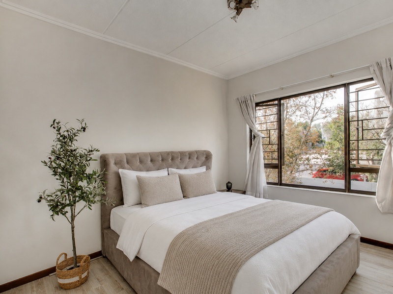 A well-lit bedroom featuring neutral walls, laminate flooring, a built-in wardrobe, and a window with security bars overlooking the exterior.