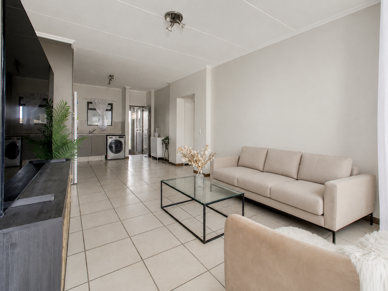 An open-plan living area featuring neutral tiled flooring, a functional kitchen space with built-in cabinetry, and integrated laundry appliances.