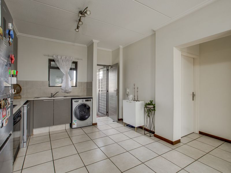 A functional kitchen featuring tiled flooring, neutral cabinetry, a tiled backsplash, and direct access to an adjacent hallway.