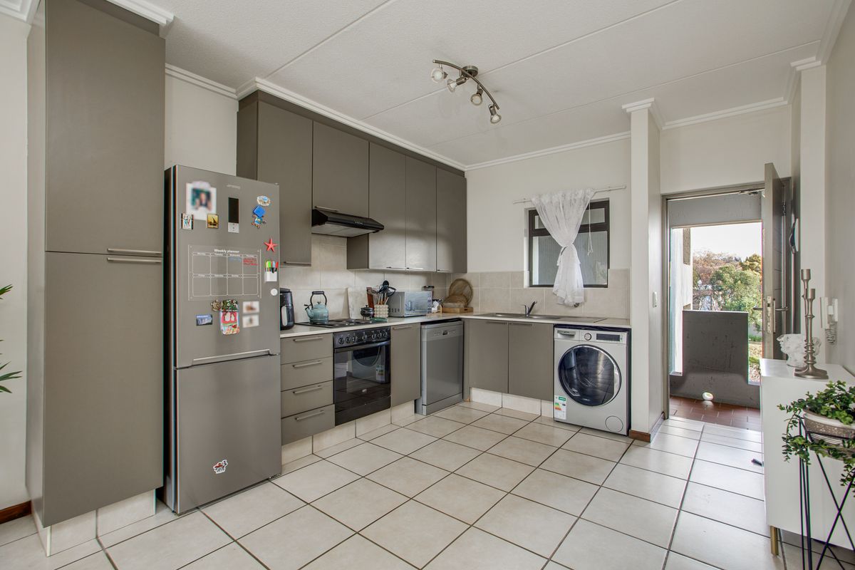 A functional kitchen featuring modern grey cabinetry, tiled flooring, built-in oven and hob, and direct access to an outdoor balcony area.
