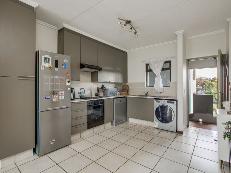 A functional kitchen featuring modern grey cabinetry, tiled flooring, built-in oven and hob, and direct access to an outdoor balcony area.