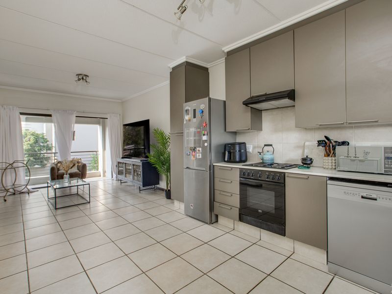 Open-plan living area featuring a modern kitchen with built-in cabinetry, oven, and hob, flowing into a bright lounge with access to a balcony.