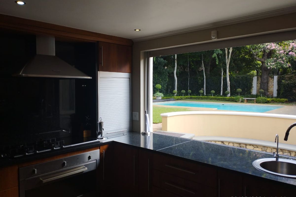 Modern kitchen featuring dark granite countertops, built-in oven, and gas hob, with a large window offering direct views of the swimming pool and garden.