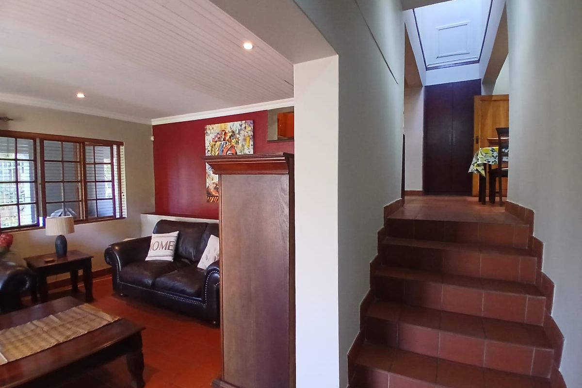 A living area featuring terracotta floor tiles, a tongue and groove ceiling with recessed lighting, and a staircase leading to an upper level with a skylight.