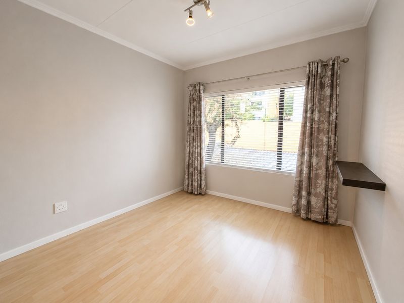 A bright, empty bedroom featuring light laminate flooring, a ceiling-mounted spotlight, and a convenient floating shelf near the window.